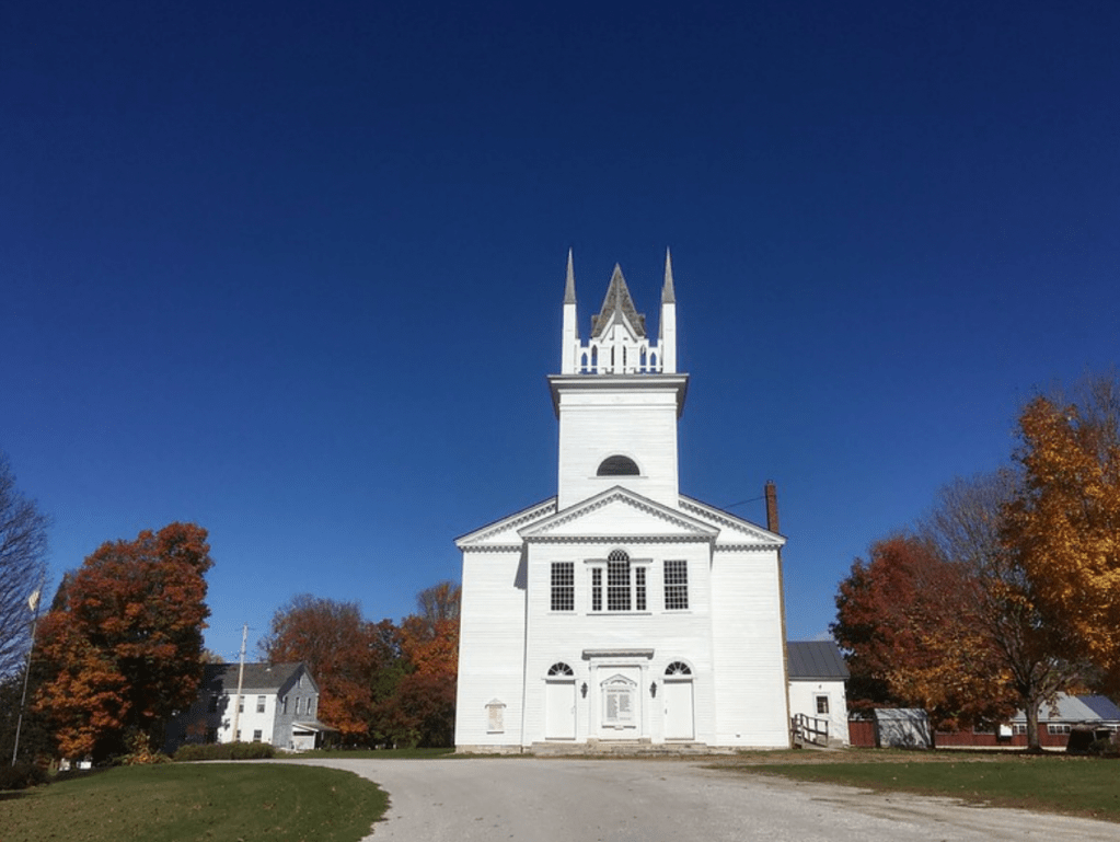 A view of the Sudbury meeting house from the front on a clear blue day